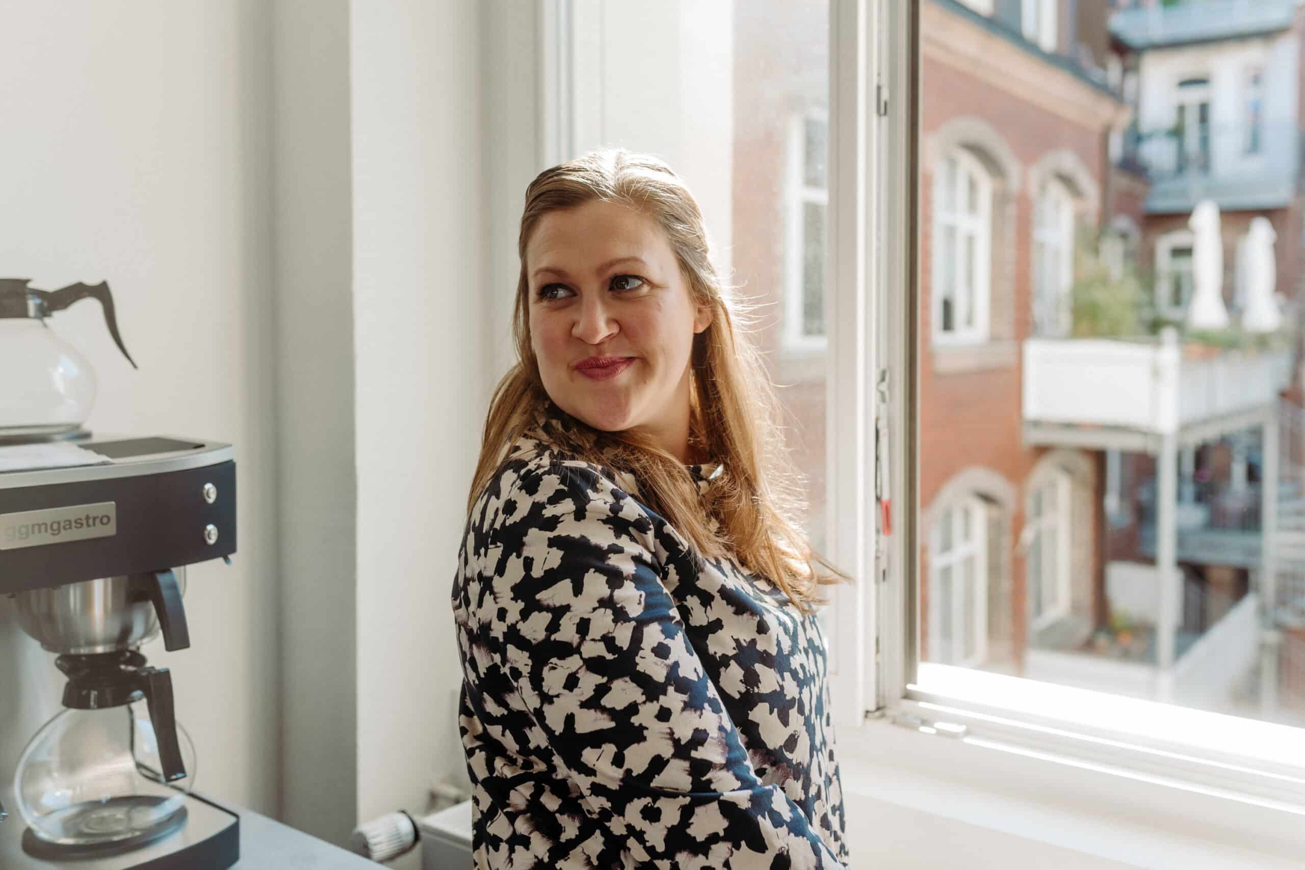 Karin steht lächelnd am Fenster und genießt die Pause.